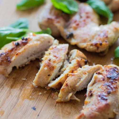 closeup of sliced grilled chicken with basil leaves.