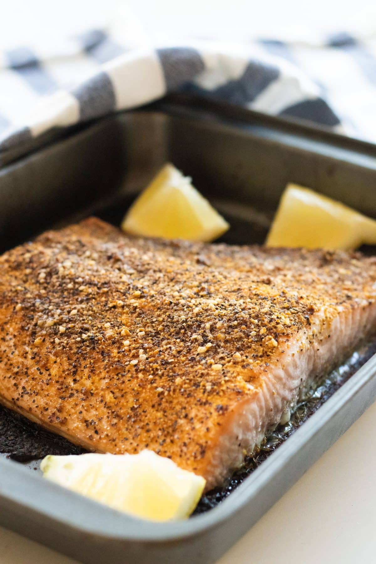 oven baked salmon covered with lemon pepper in an oven pan with lemon wedges