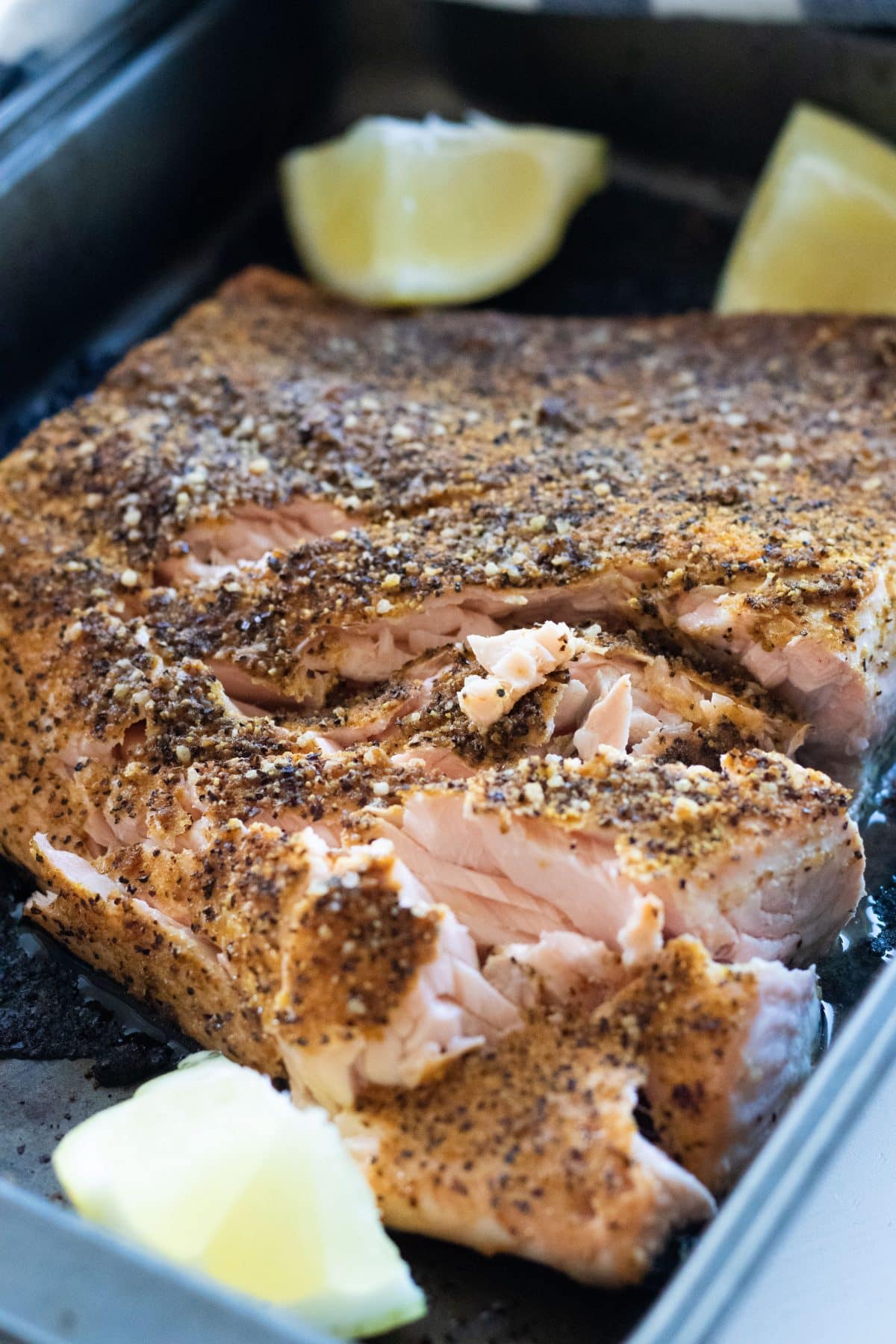 oven baked lemon pepper salmon in an oven pan with lemon wedges.