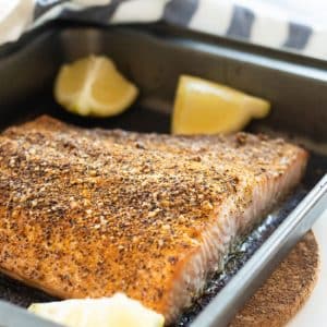 oven baked lemon pepper salmon in an oven pan with lemon wedges