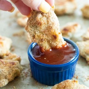 sideview of a chicken tender being dipped in barbecue sauce