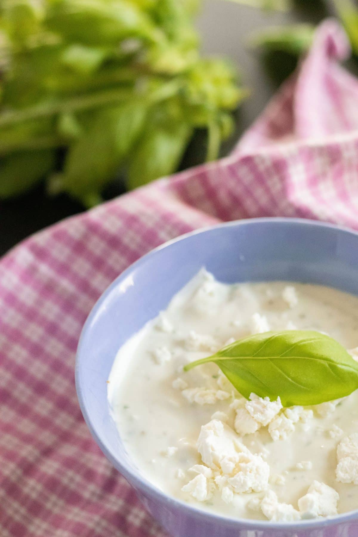 whipped feta cheese in a blue bowl with a fresh basil leaf, on top of a pink and white kitchen towel with fresh basil in the background