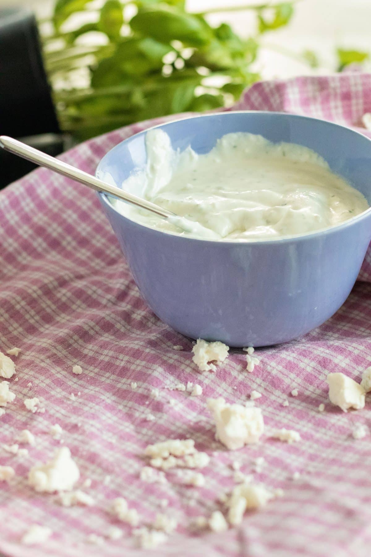 a bowl of whipped feta cheese with a spoon in front of crumbled feta cheese on a kitchen towel