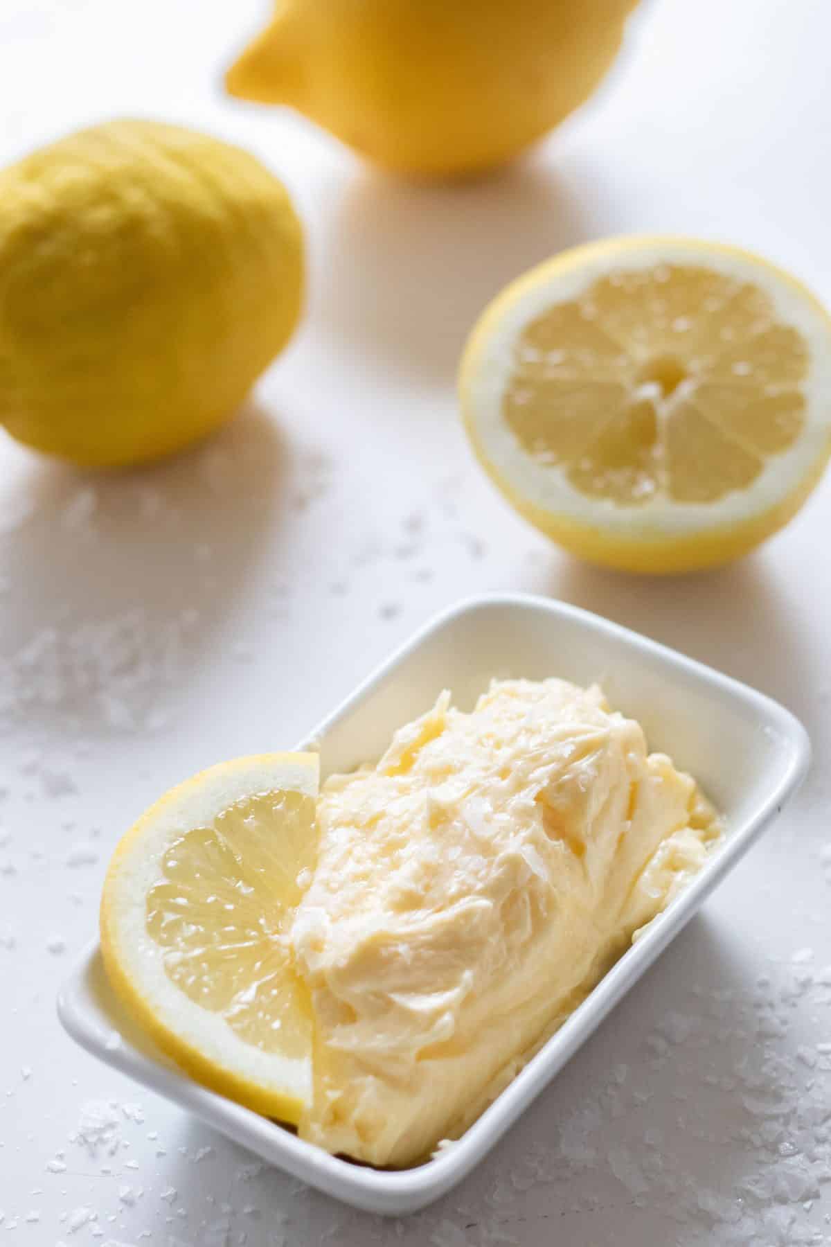 side top view of whipped lemon butter in a rectangular bowl with a lemon slice and lemons in the background.