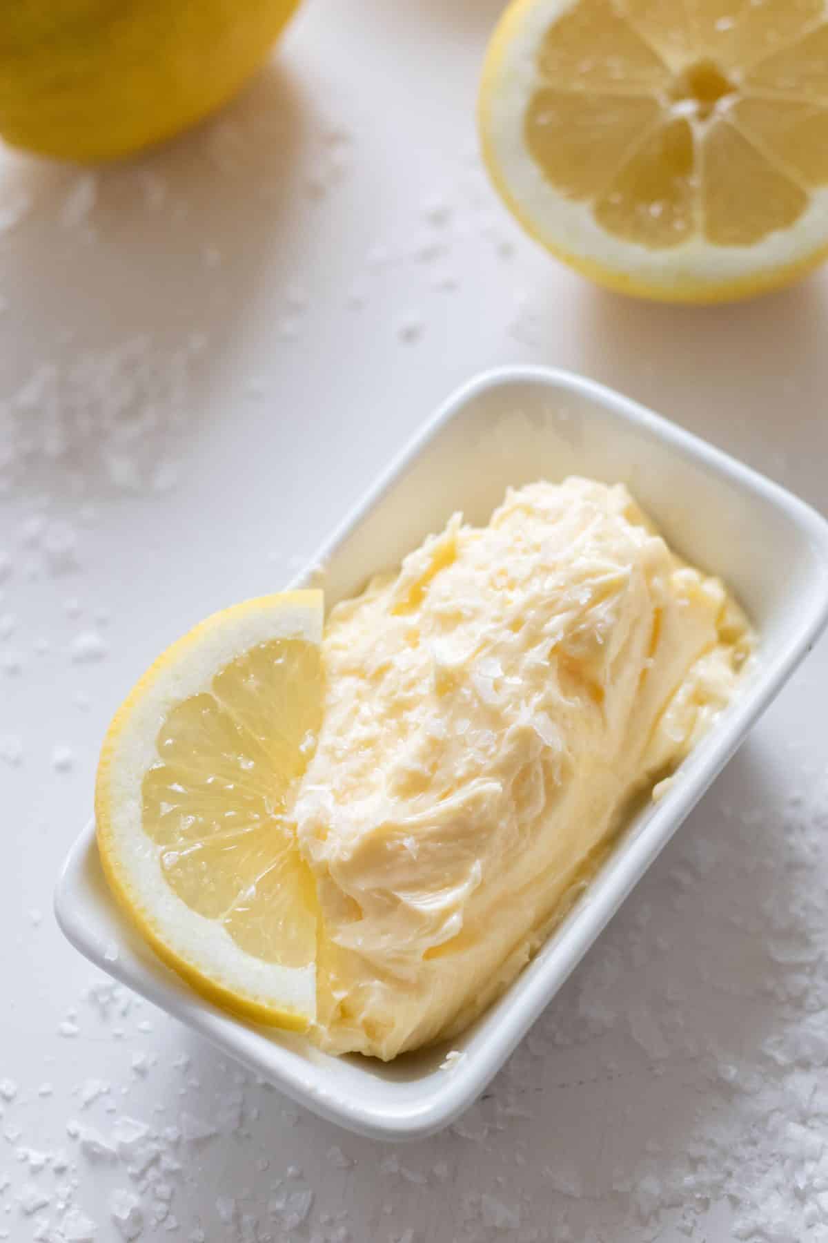 top view of whipped lemon butter in a rectangular bowl with a lemon slice and lemons in the background