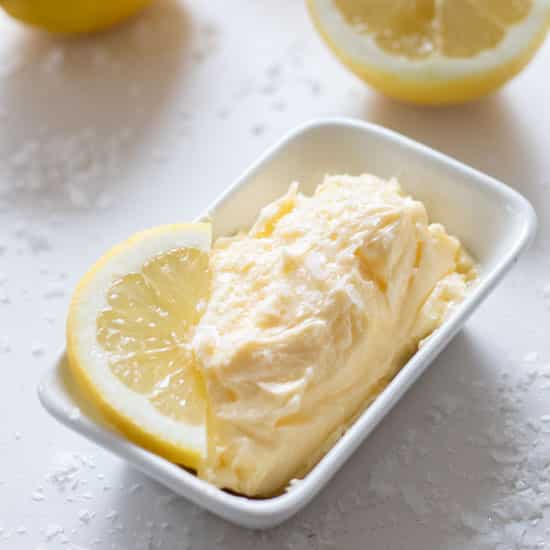 side top view of whipped lemon butter in a rectangular bowl with a lemon slice and lemons in the background