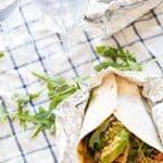 wrap with halloumi, avocado and arugula and two plastic wine glasses with water on top of a checkered picnic blanket