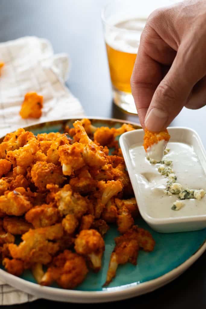 a buffalo cauliflower wing being dipped into blue cheese sauce