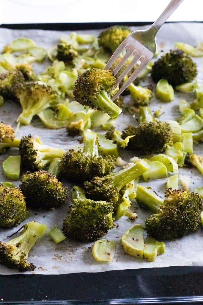 taking a piece of garlic roasted broccoli from an oven tray with a fork