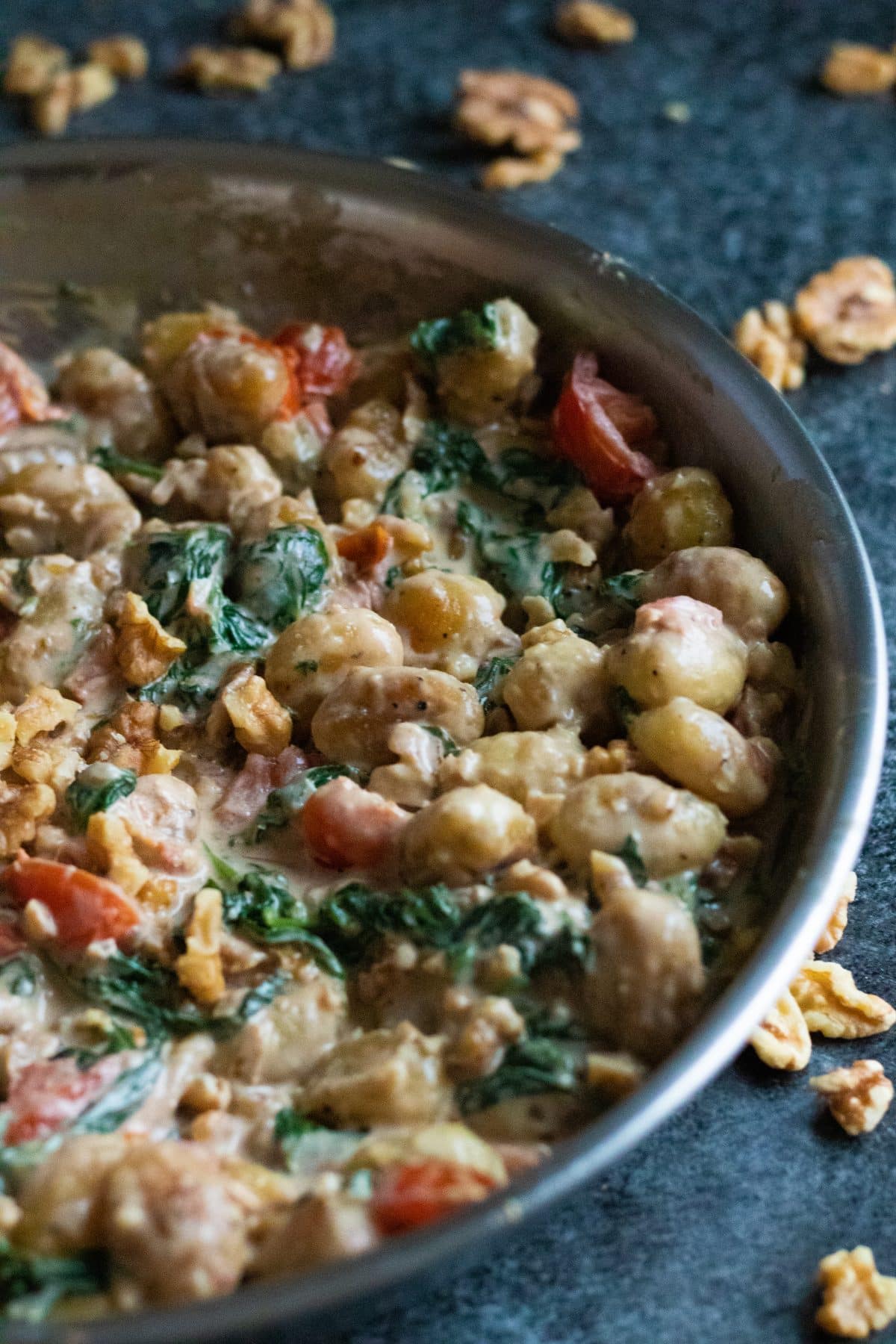 side view of a pan with creamy gnocchi with gorgonzola, and walnuts in the background.