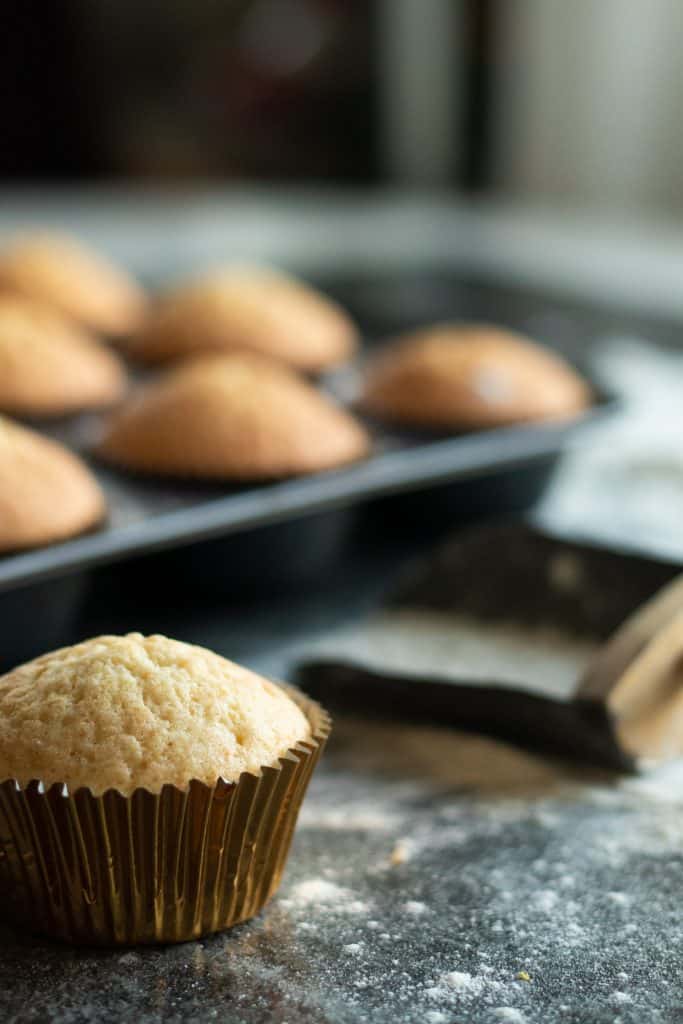 side view of a vanilla muffin in front of a tray of vanilla muffinsin