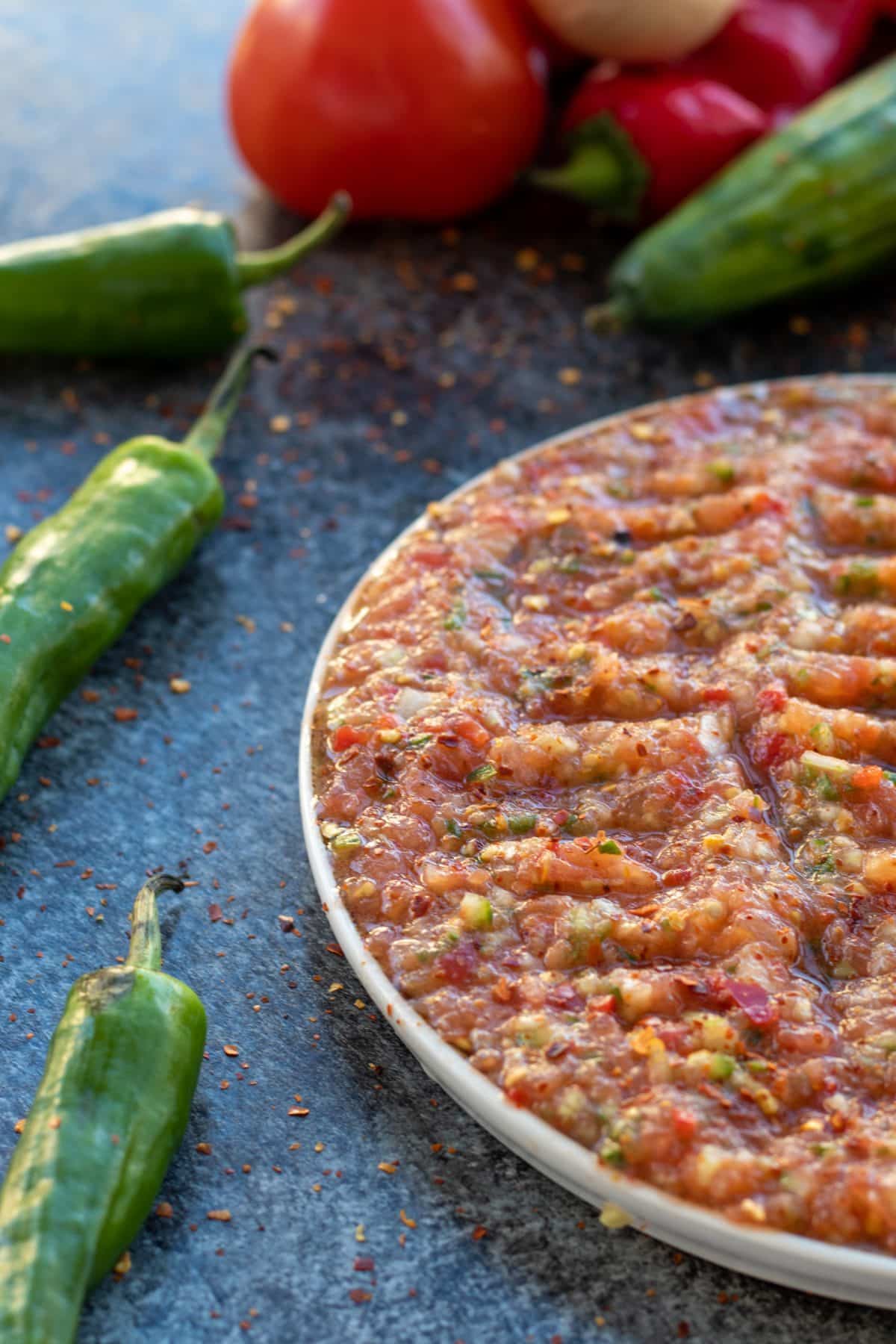 side view of acili ezme on a plate with green peppers on the side.