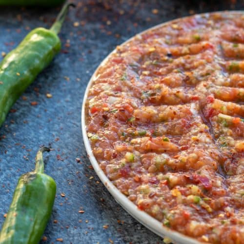 side view of acili ezme on a plate with green peppers on the side