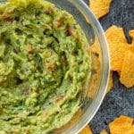 top down view of a bowl of guacamole with tortilla chips on the side
