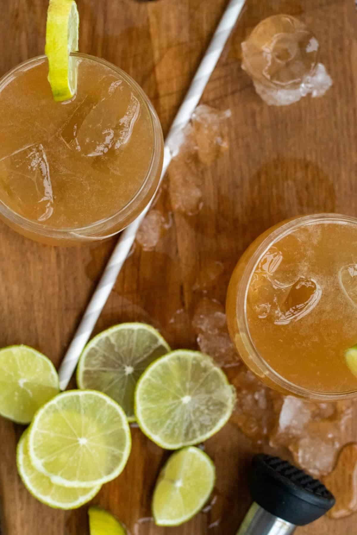 top down view of two kentucky mule cocktails on a wooden chopping board with a straw and lime slices