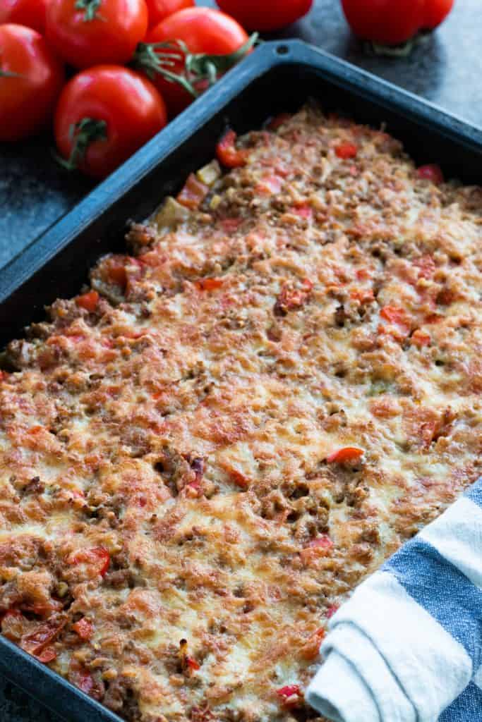 moussaka with a golden cheese crust in an oven tray, with some tomatoes in the background