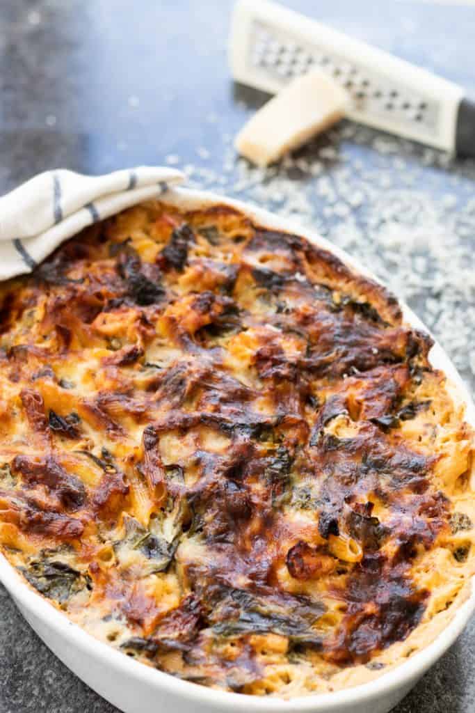 finished pasta bake with sun-dried tomatoes and spinach with a piece of parmesan in the background