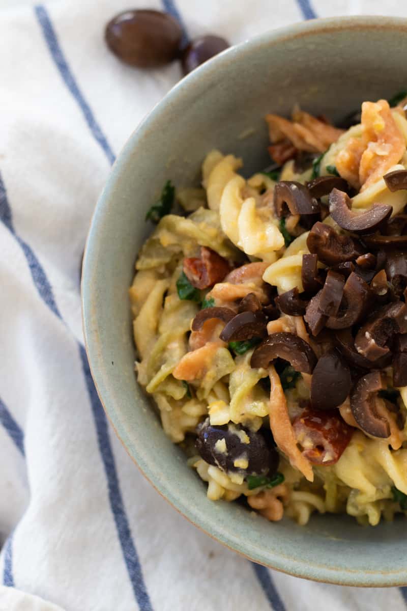 top down view of a bowl of hummus pasta on top of a white and blue kitchen towel