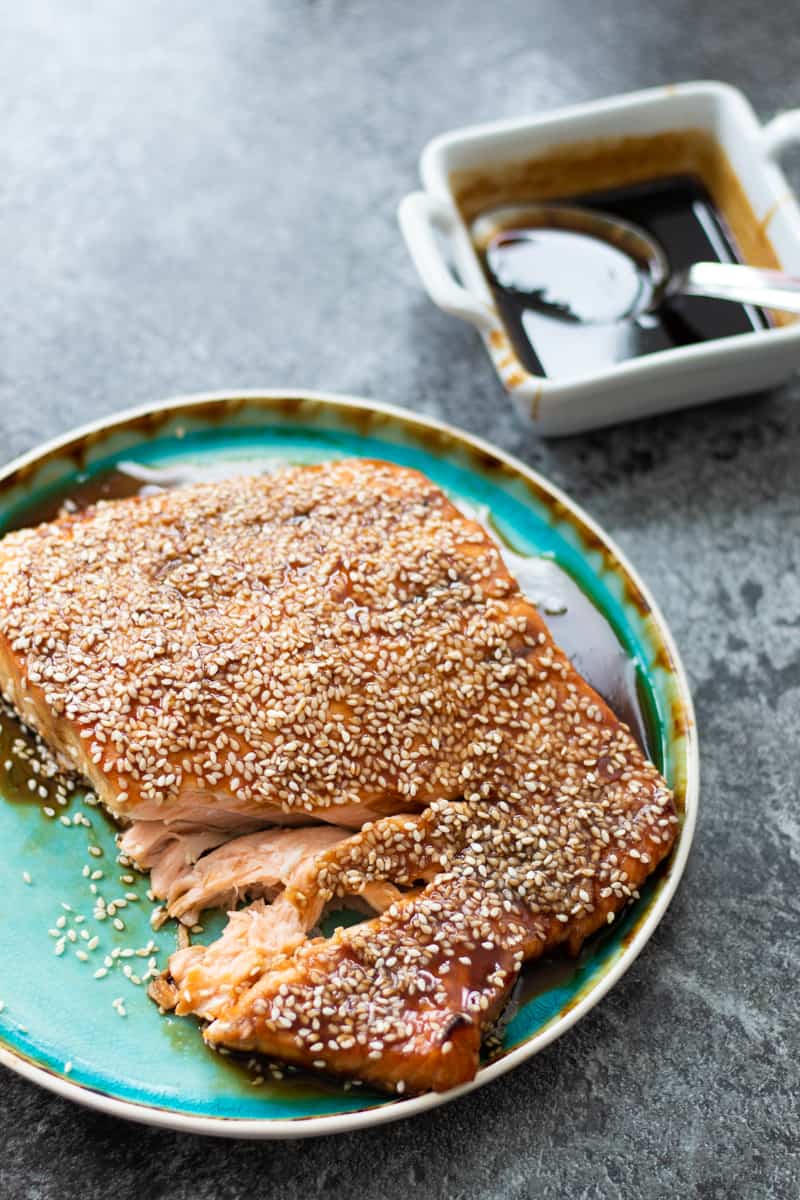 side view of baked teriyaki salmon on a turquoise plate with a bowl of teriyaki sauce in the background