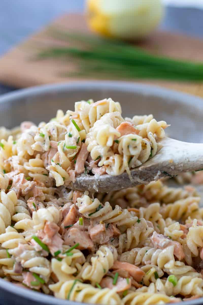 a spoonful of salmon creme fraiche pasta on top of a pan full, with chives anda  lemon on a chopping board in the background