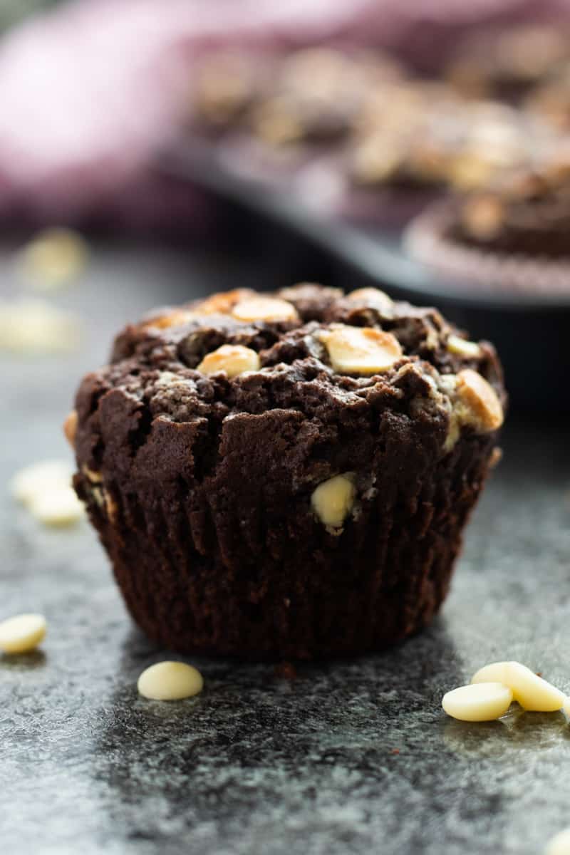 side view of a double chocolate chip muffin in front of a muffin tray full