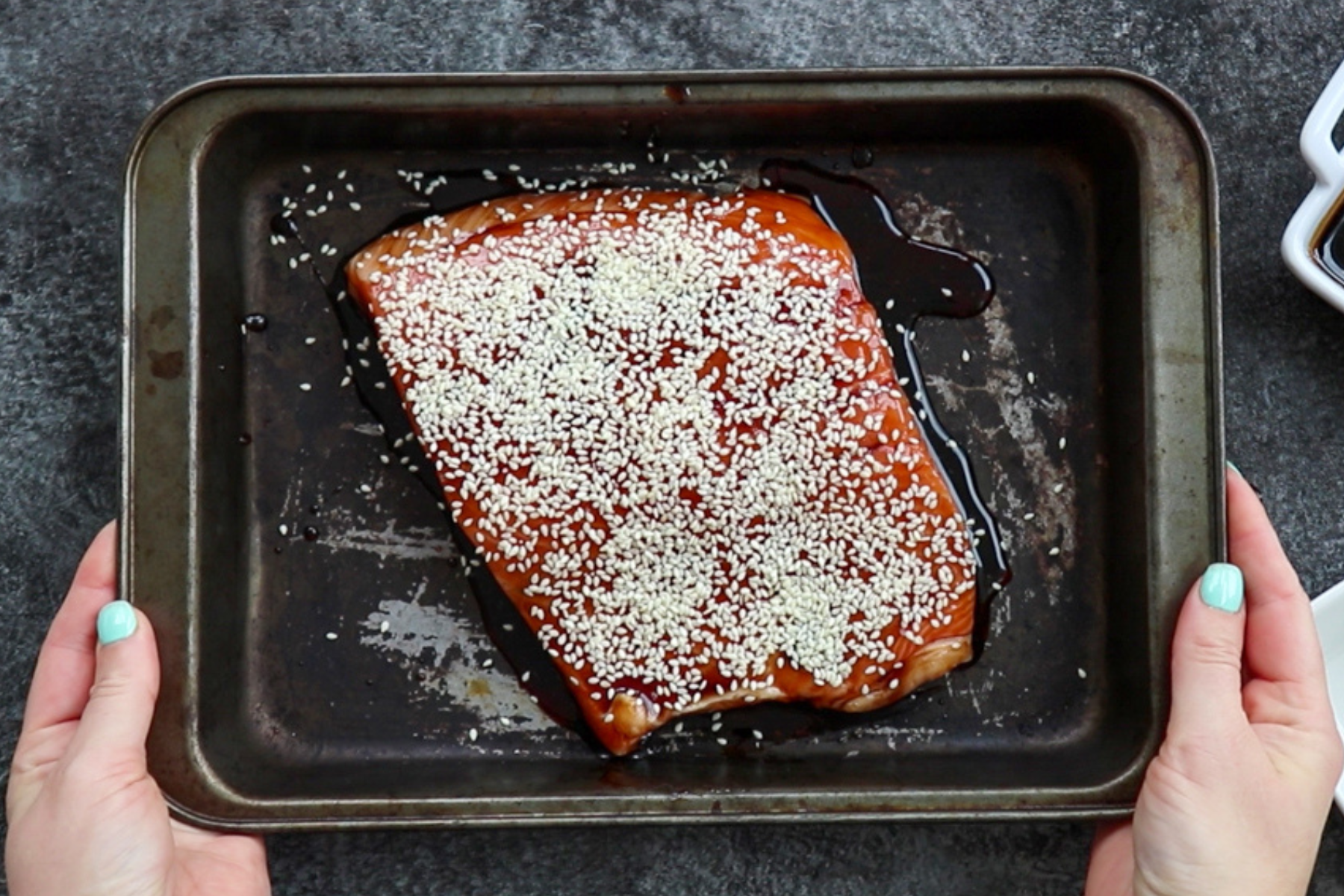 Teriyaki salmon in a pan topped with sesame seeds, before baking.