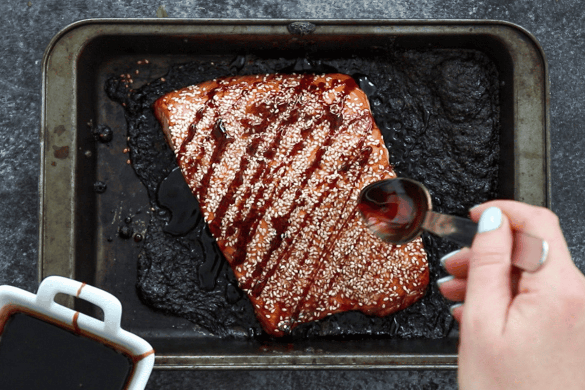 Drizzling teriyaki sauce over finished baked teriyaki salmon topped with sesame seeds.