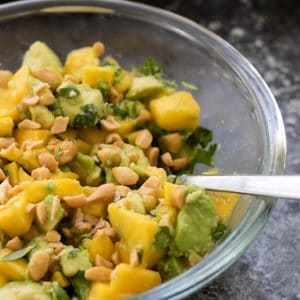 side view of a bowl of avocado mango salad with salted roasted peanuts and some sea salt flakes in the background