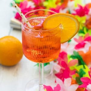 side view of an aperol spritz garnished with orange, with an orange nd some plastic flowers around it