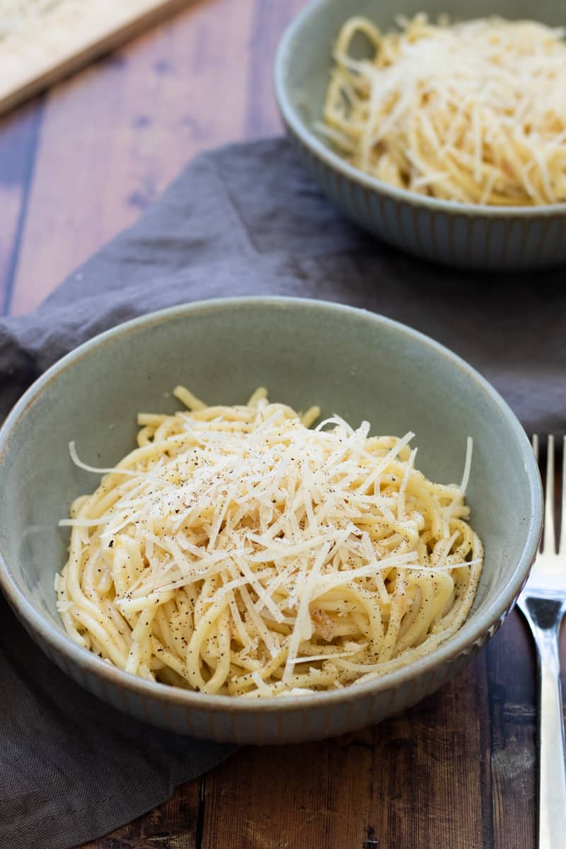 side view of a bowl of garlic butter pasta topped with parmesan cheese and fresh ground black pepper