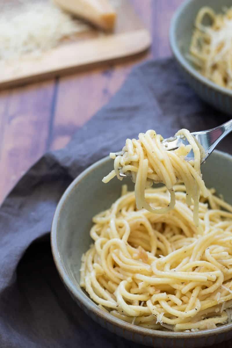 a forkful of garlic butter spaghetti lifted up over a bowl full, with parmesan cheese in the background