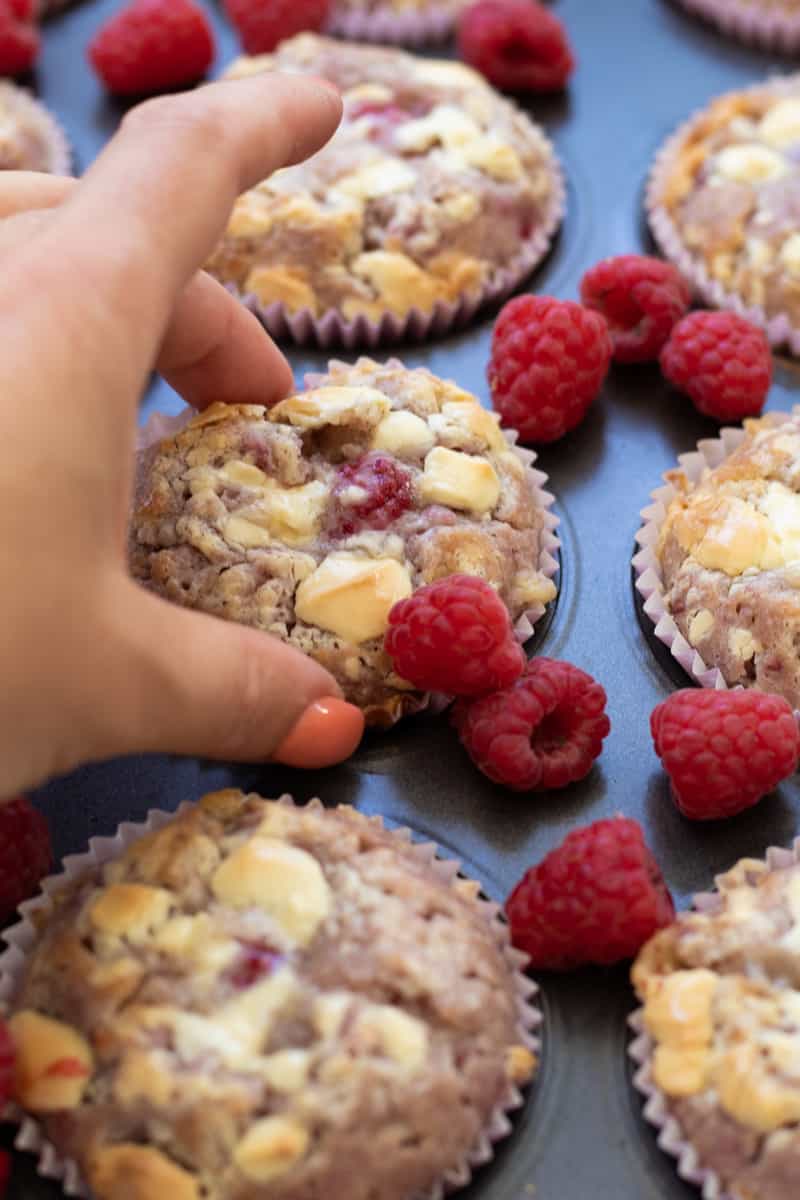 a raspberry white chocolate muffin being picked up from a tray full