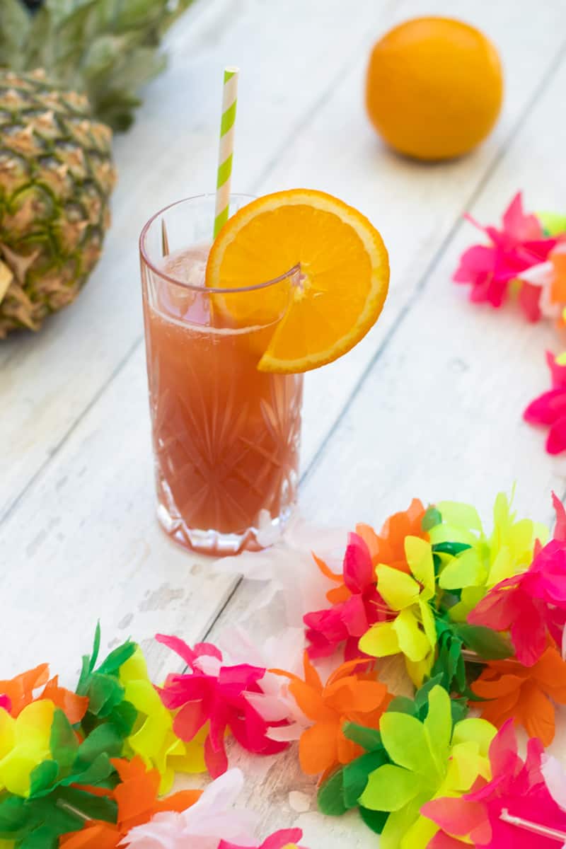 sex on the beach mocktail decorated with a slice of orange with an orange and a pineapple in the background