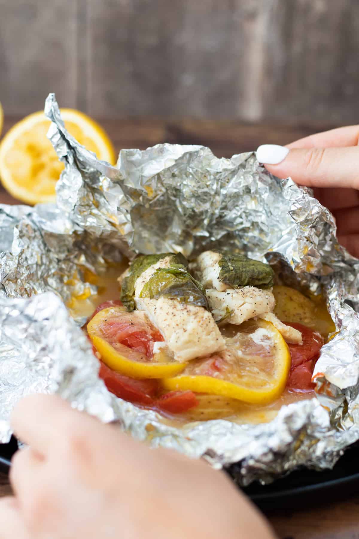 a foil pack with cod, potatoes, tomatoes and lemon being opened after cooking.