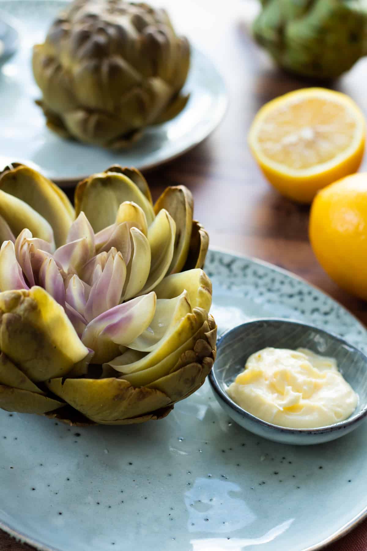 side view of a boiled artichoke on a blue plate.