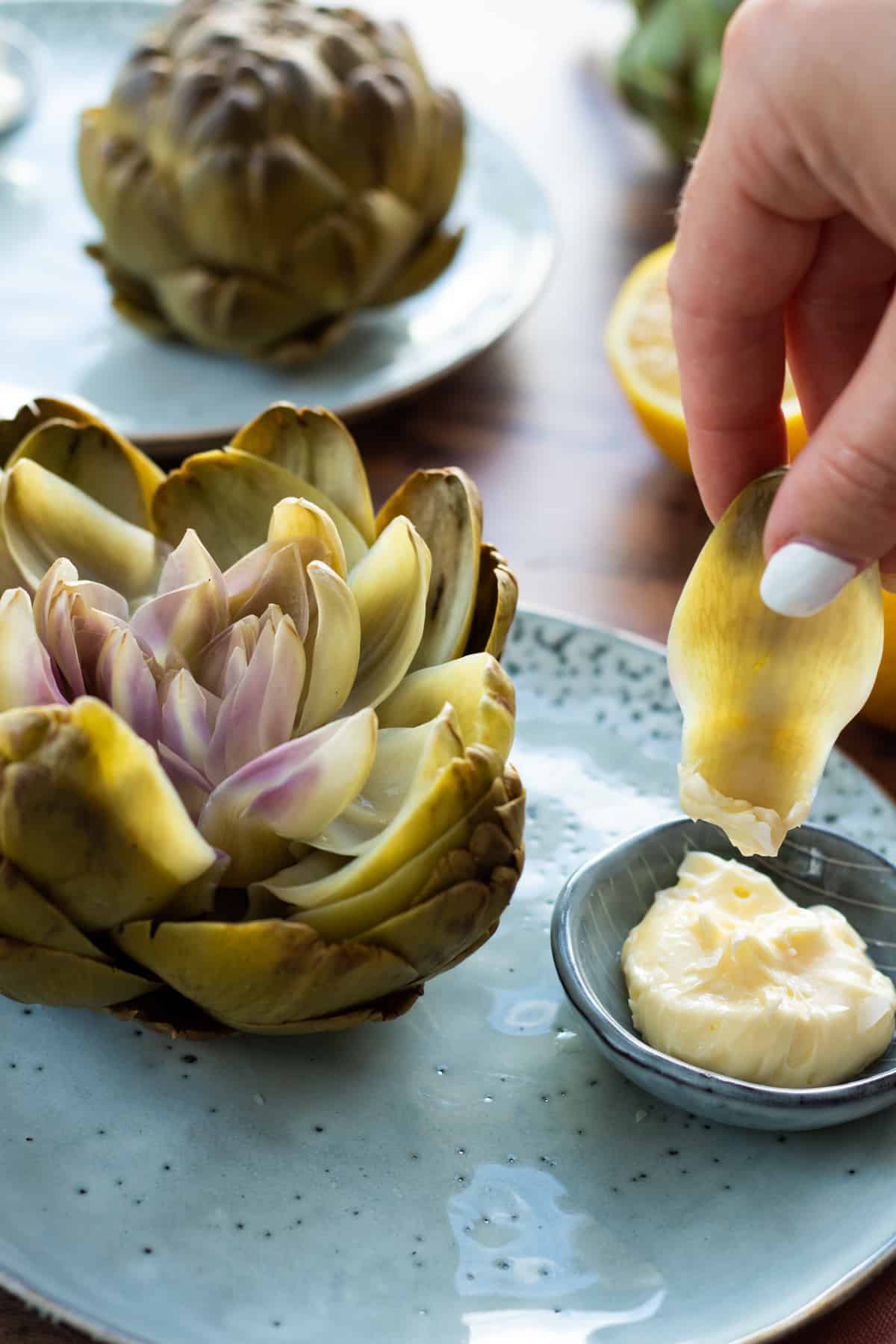 an artichoke leaf being dipped into whipped lemon butter next to a whole artichoke