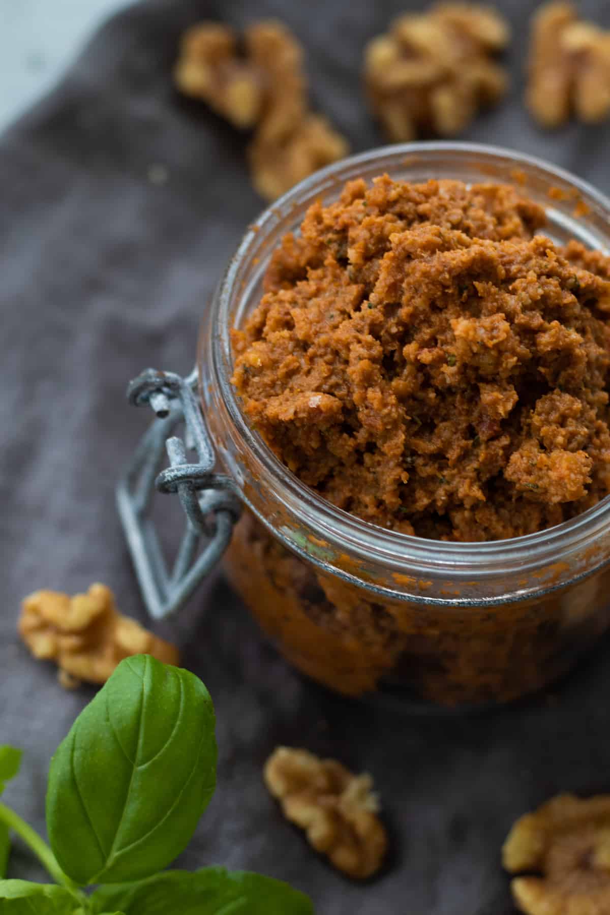 red pesto  in a jar with walnuts and basil around.