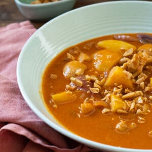a bowl full of massaman chicken curry topped with chopped peanuts