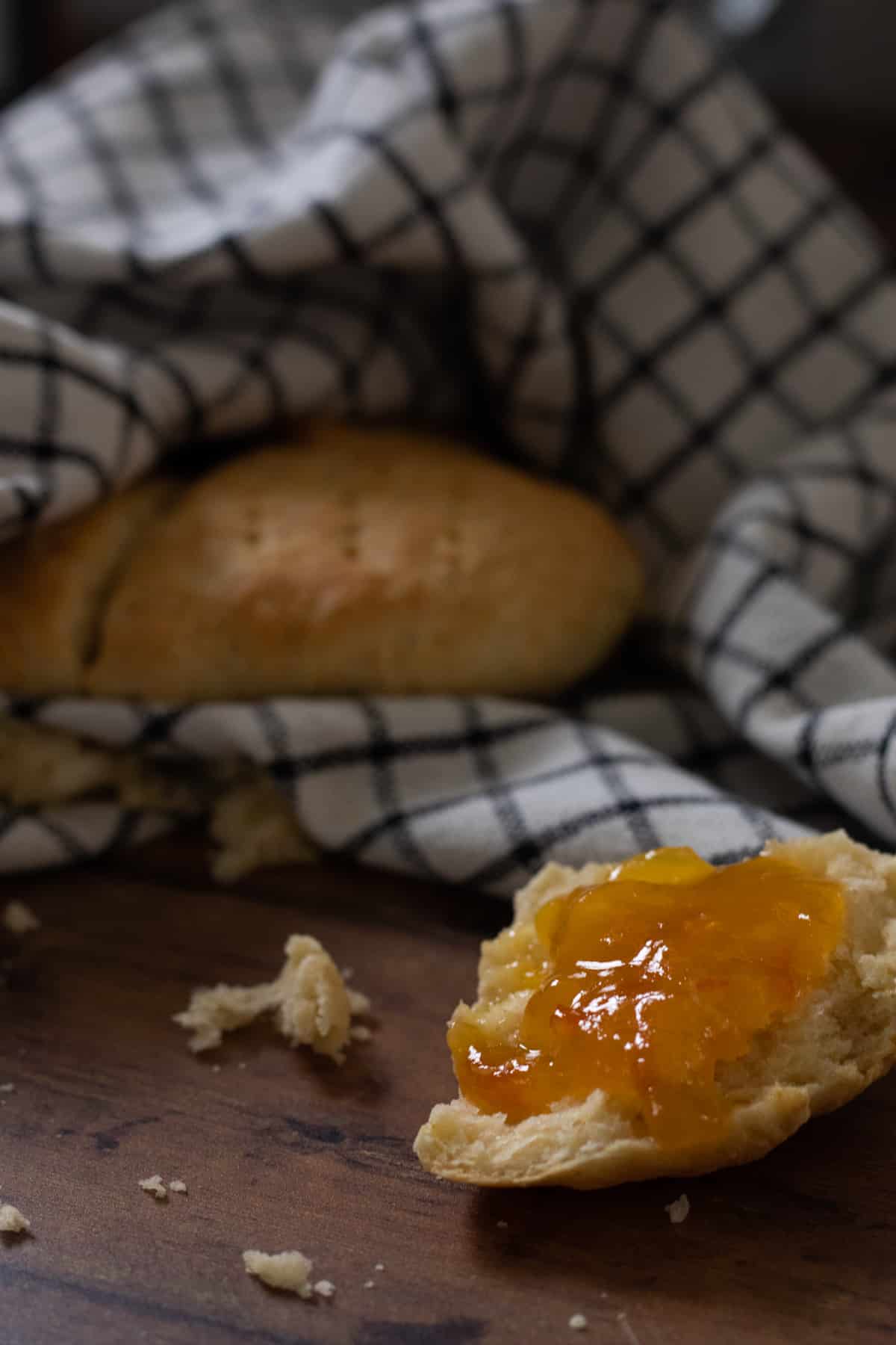 a scone topped with marmalade in front of scones wrapped in a kitchen towel.