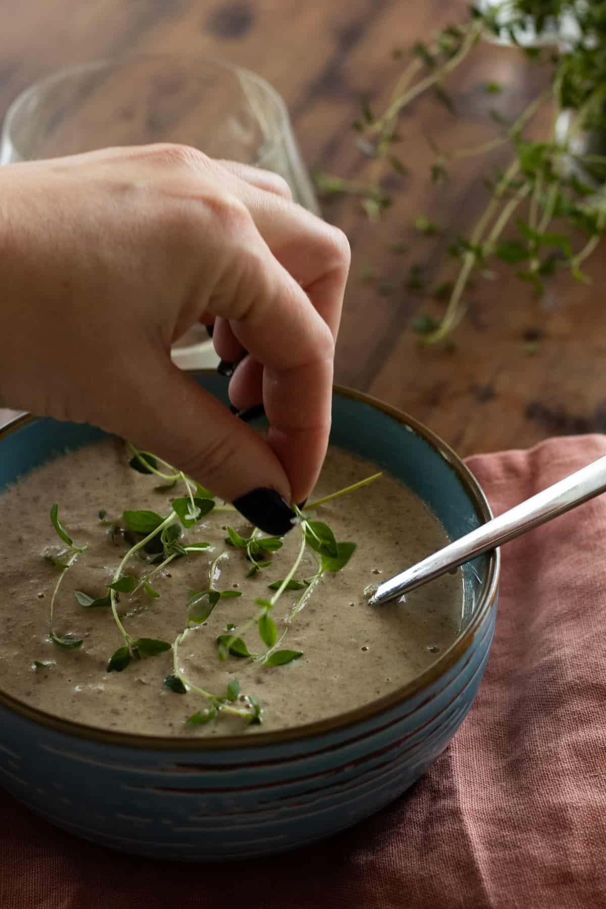 green herbs being placed on top of a bowl of cream of mushroom soup