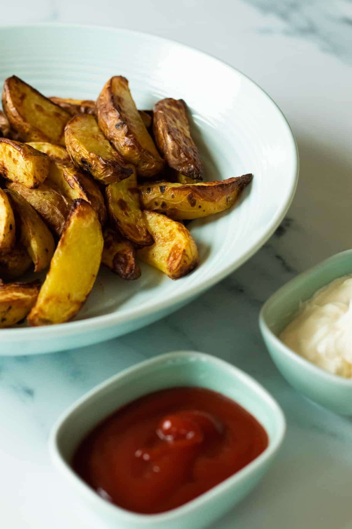 potato wedges in a bowl next to two dip sauces