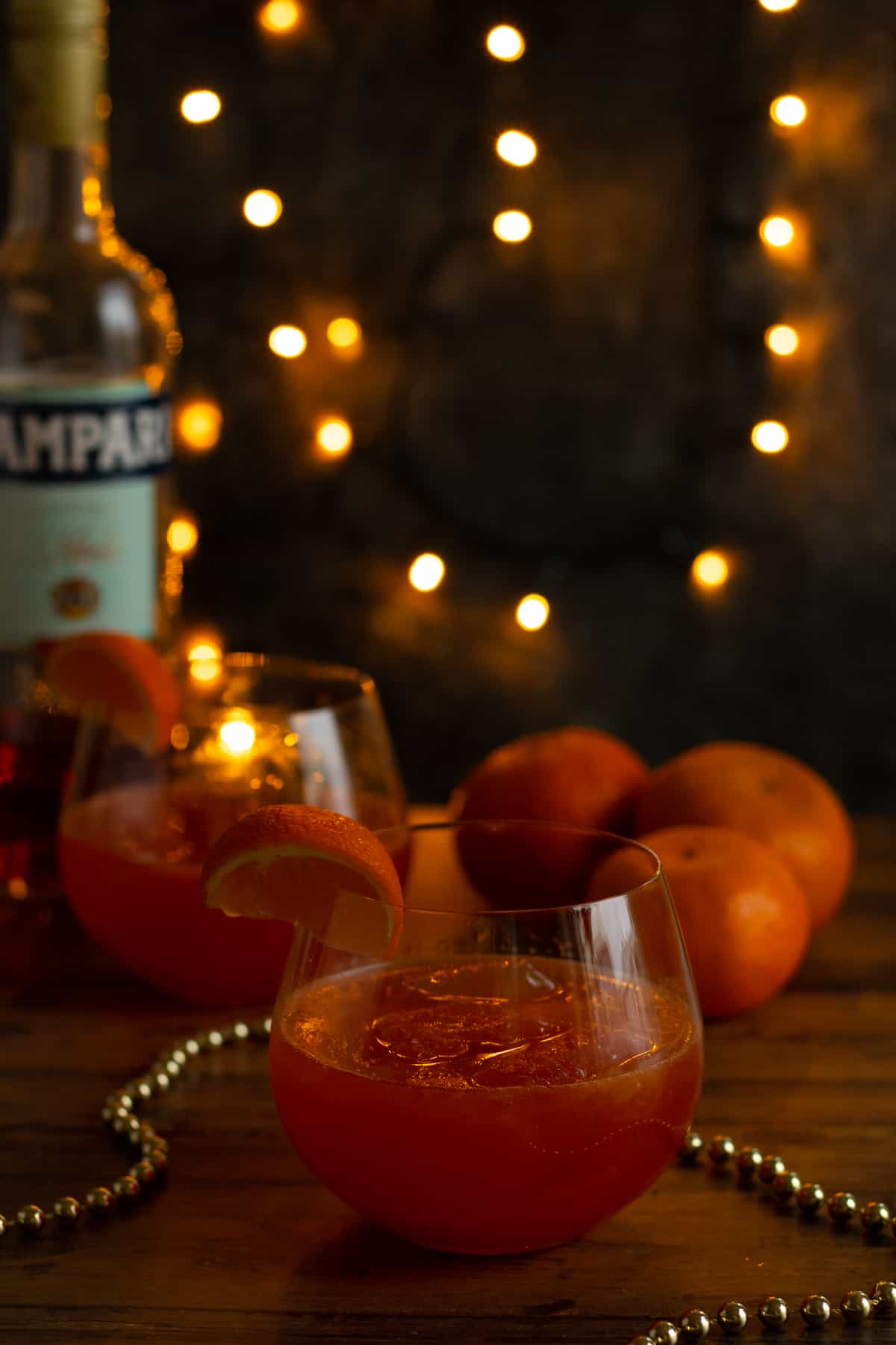 a clementine campari spritz with clementines and a bottle of campari in the background