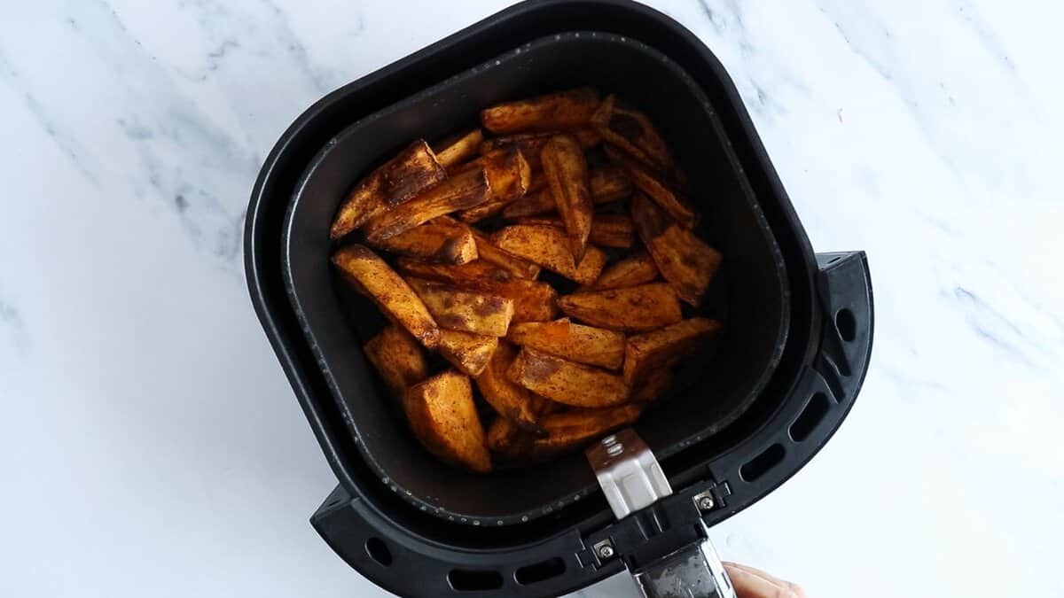 Air fryer sweet potatoes seasoned with salt, cinnamon and olive oil in an air fryer basket after cooking.
