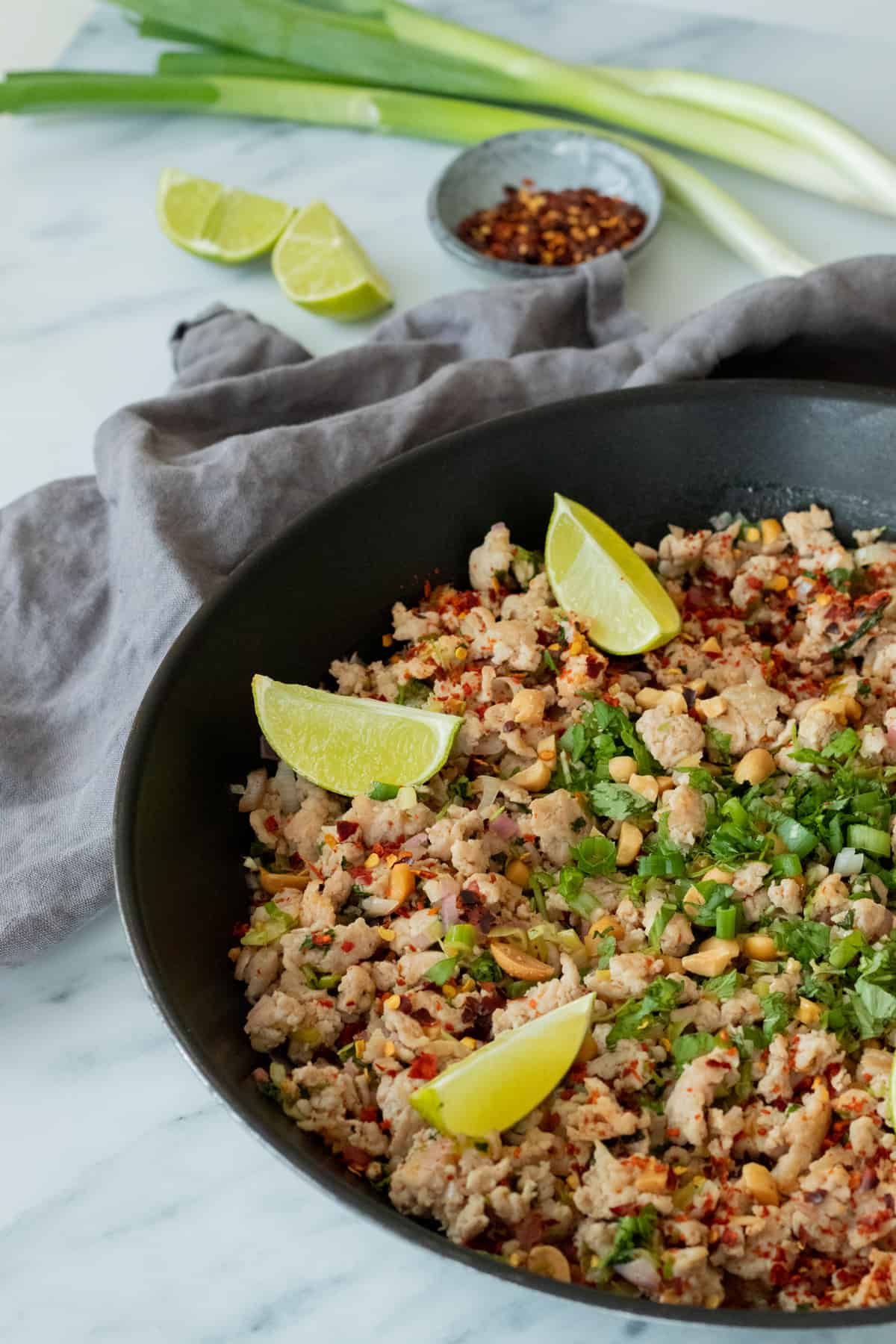 larb gai in a pan, decorated with lime wedges