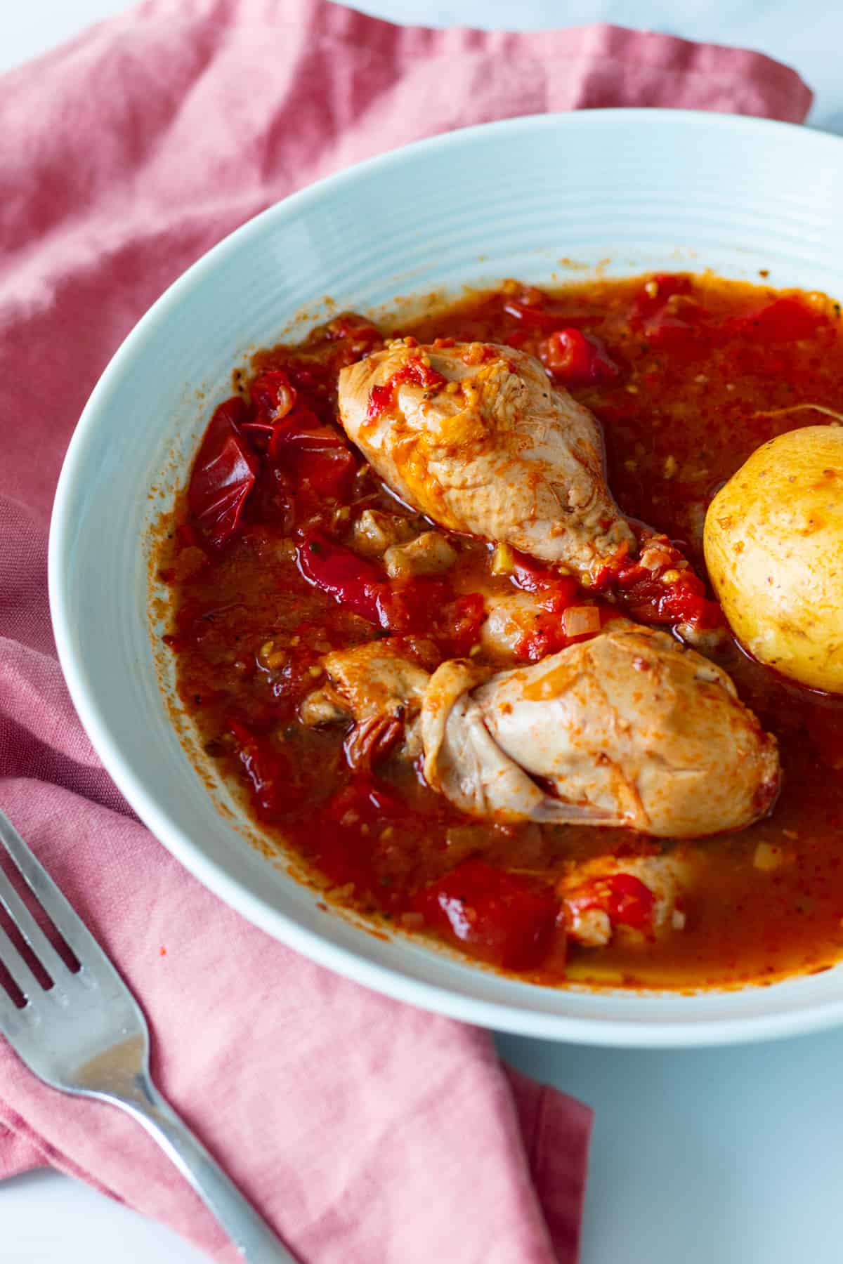 chicken and potatoes with tomato sauce in a blue bowl