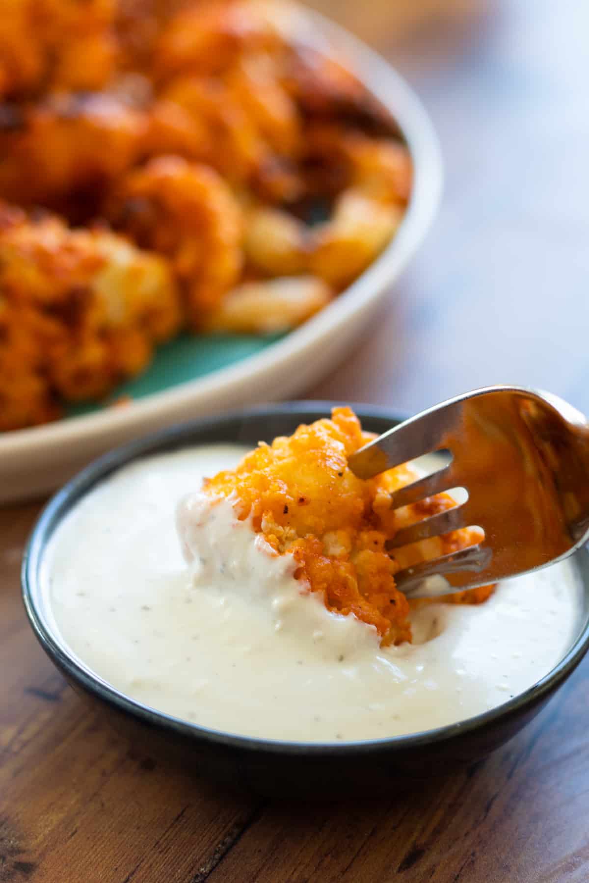 a piece of buffalo cauliflower being dipped in blue cheese sauce