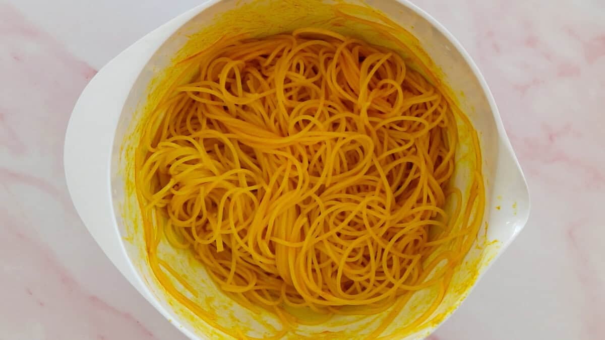 A bowl with rice noodles mixed with turmeric and oil.