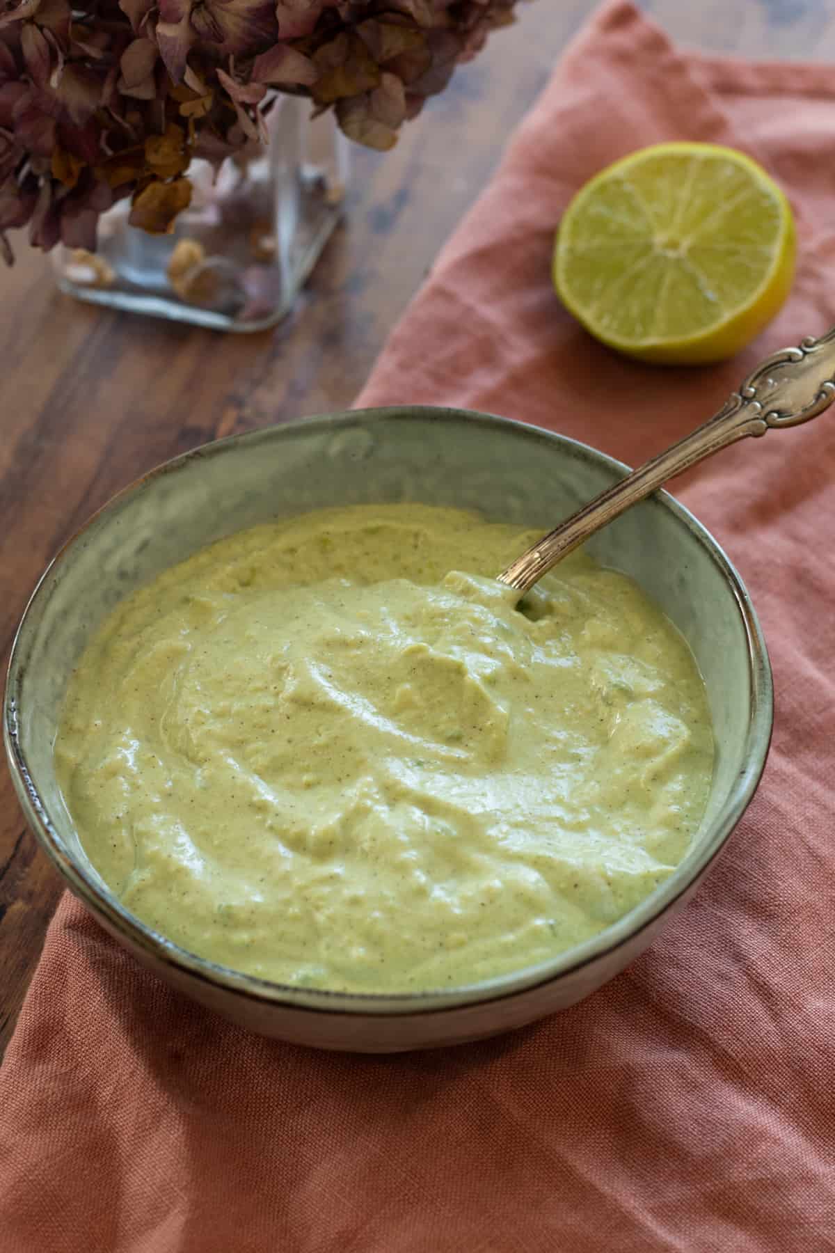 sour cream sauce with avocado and lime in a blue bowl with a spoon