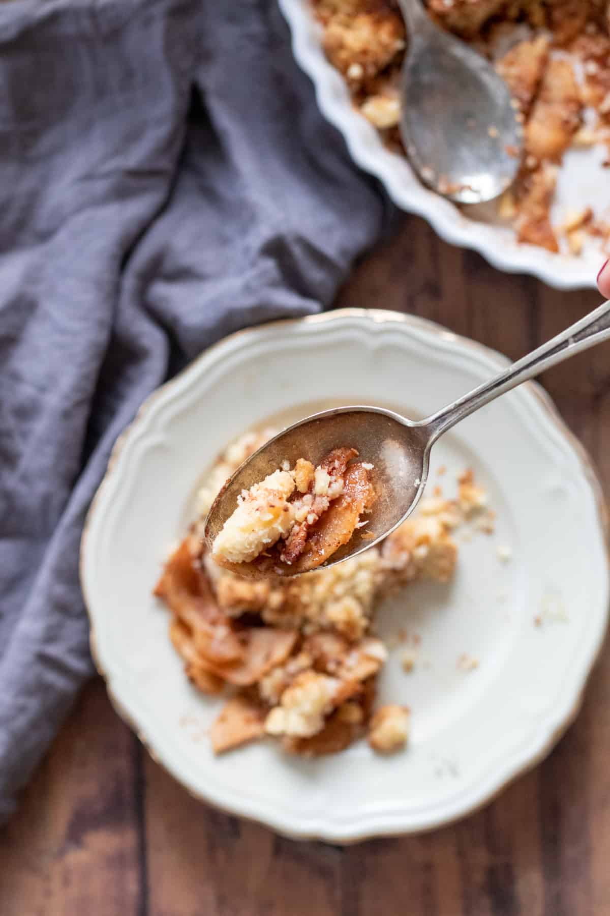apple crisp without oats on a white plate with a spoonful lifted above.