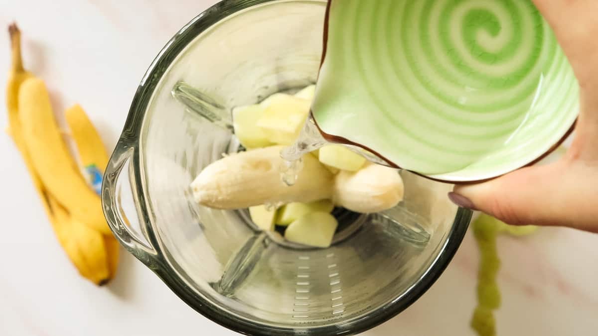 Apple and banan in a blender with water being poured in.